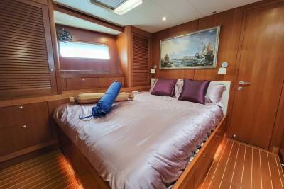 Luxurious wood-paneled stateroom aboard a yacht features a plush bed adorned with satin linens and decorative pillows.