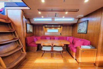 A warm, wood-paneled salon with a U-shaped crimson sofa and a central dining table offers a cozy gathering space on this yacht.