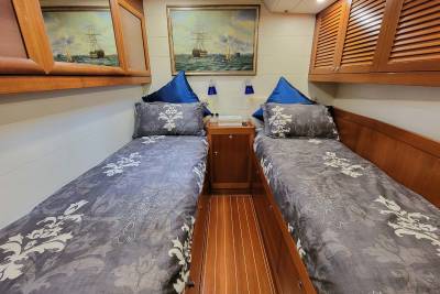 Two cozy beds with ornate grey bedding and blue pillows are nestled between wooden cabinets, creating a nautical-themed cabin.