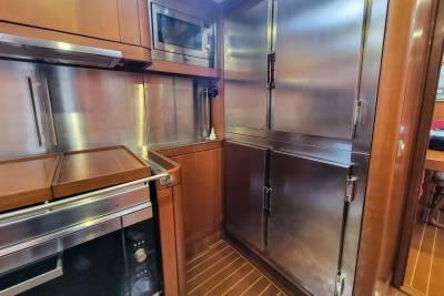 A galley kitchen on a boat features stainless steel appliances and warm wood cabinetry.
