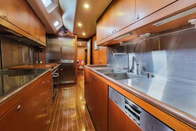 The galley of this yacht features warm wood cabinetry, a stainless steel backsplash, and a double sink with a modern faucet.