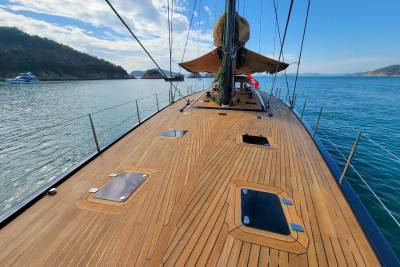 The polished wooden deck of a sailboat stretches towards the horizon under a bright blue sky dotted with clouds.