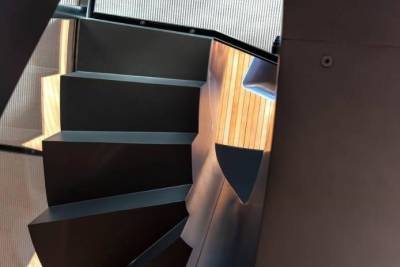 A modern spiral staircase with dark metal steps curves elegantly upwards towards a textured, arched window.