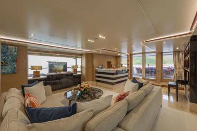 A luxurious yacht interior features a spacious lounge with a bar, comfortable seating, and large windows overlooking an outdoor deck.
