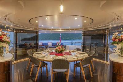 An elegant yacht dining room is set for a formal meal with a stunning view of the ocean and surrounding landscape.