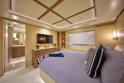 Luxurious yacht bedroom features a king-size bed with striped linens, a wall-mounted television, and an adjoining elegant bathroom.