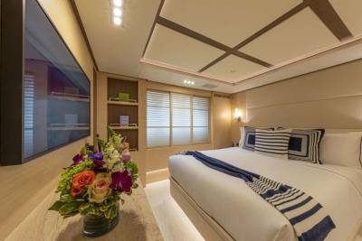 A luxurious yacht bedroom features a large bed with striped pillows and a cozy blue throw, complemented by a vibrant floral arrangement.