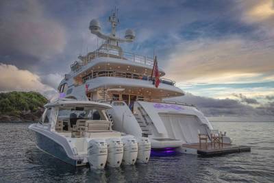 A luxurious mega-yacht with a tender boat attached floats serenely in calm waters under a dramatic sunset sky.
