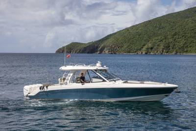 A man pilots a sleek blue and white boat through calm waters with a lush green island in the background.