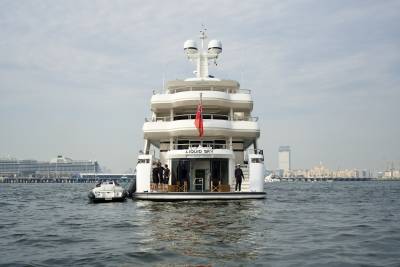 A grand yacht named Liquid Sky is docked in a harbor with a city skyline in the background.