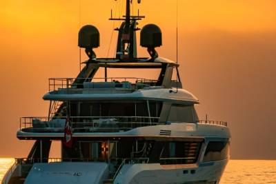 A luxurious yacht glides across the golden ocean waters at sunset.