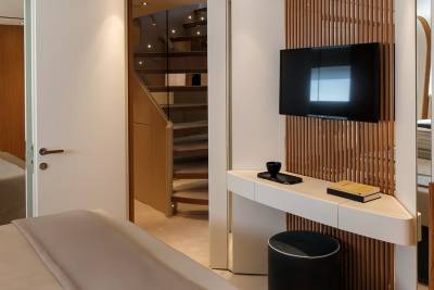 A modern bedroom features a sleek vanity, a television, and a view of a curved staircase.