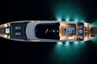 An aerial view captures a luxurious yacht illuminated by underwater lights, showcasing its sleek design and inviting deck spaces.