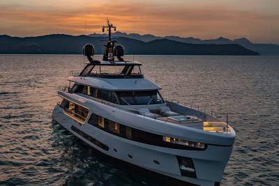 A luxurious yacht glides across calm waters at sunset, with silhouetted mountains in the distance.
