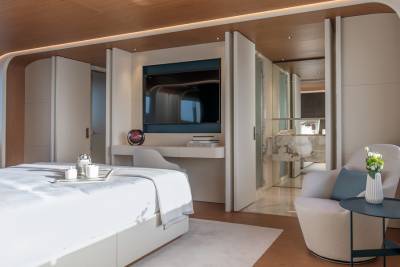 Luxurious yacht interiors offer a serene bedroom with a sleek entertainment center and an adjacent spa-like bathroom.