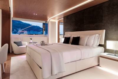 Luxurious yacht bedroom features a king-sized bed, modern desk, and stunning ocean views through a panoramic window.