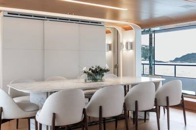 Dine in modern elegance aboard this yacht, with a marble table and plush chairs overlooking a serene coastal landscape.