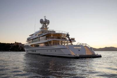 A luxurious superyacht named "New Secret" glides through calm waters at dusk, illuminated by warm lights.