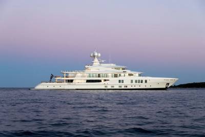 A luxurious white yacht glides across calm waters under a dusky purple and blue sky.