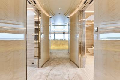 A luxurious, curved hallway with polished marble walls and a plush carpet leads to a brightly lit lounge area.