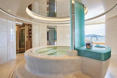 Luxurious spa on a yacht features a marble jacuzzi and a striking blue glass vanity overlooking the ocean.