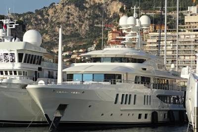 Luxurious white yachts are docked in a harbor with a mountainous backdrop under a clear blue sky.