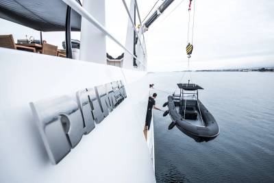 A crew member guides a black inflatable boat being lowered by a crane from a large white yacht.