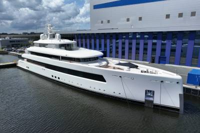 A sleek white superyacht is docked beside a modern industrial building with blue accents.