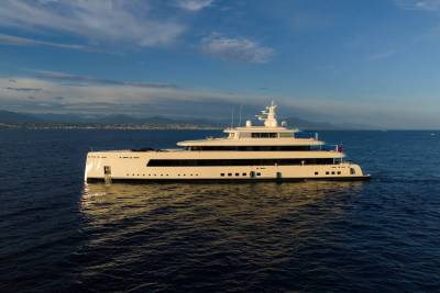 A luxurious white yacht glides serenely on the deep blue sea under a partly cloudy sky with distant mountains.