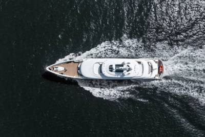 A sleek white yacht cuts through dark, rippling water, leaving a foamy white wake in its path.