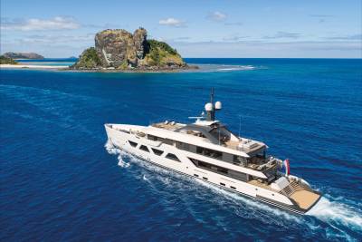 A luxurious white yacht cruises through the vibrant blue ocean near a rocky, verdant island.