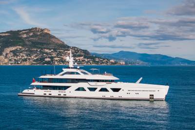 A luxurious white yacht cruises serenely on the azure waters off a picturesque coastal town nestled against rolling hills.