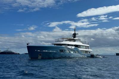 A large, luxurious yacht sits in the calm, blue waters, surrounded by a picturesque sky with fluffy white clouds.