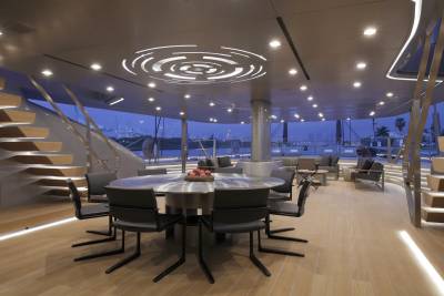 A modern yacht dining area features a sleek metal table surrounded by minimalist chairs, with a backdrop of a city skyline at dusk.