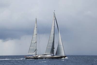 A sleek, twin-masted yacht glides through the choppy blue waters under a dramatic, cloudy sky.