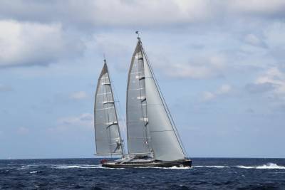 A sleek, modern sailing yacht cuts through the deep blue ocean under a cloudy sky.