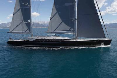 A sleek black yacht with dark grey sails glides through the azure waters under a bright blue sky.