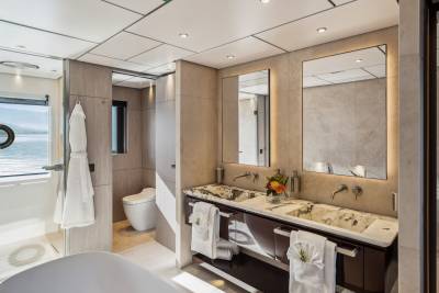 Luxurious yacht bathroom features a double vanity with marble sinks, a separate shower, and a toilet with a view of the water.
