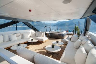 Luxurious white sofas and a hot tub offer the perfect spot to relax on this yacht's deck with a stunning mountain and sea view.