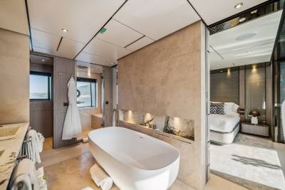 A luxurious yacht bathroom features a freestanding tub, marble accents, and a view of the ocean, adjacent to a well-appointed bedroom.