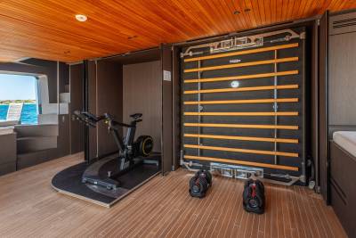 This modern yacht gym features a stationary bike, adjustable dumbbells, and a wall-mounted exercise system with a scenic ocean view.