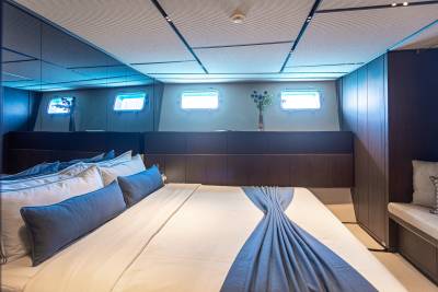 Luxurious yacht cabin features a comfortable bed with blue accents and porthole windows reflecting the serene blue light.