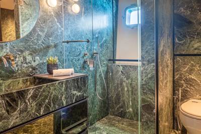 Luxurious green marble envelops this modern bathroom, featuring a sleek glass shower and a vanity with mirrored drawers.