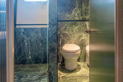 Luxurious green marble adorns this opulent bathroom, complete with a porthole window and a sleek toilet.