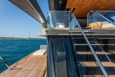Modern yacht stairs with glass railings lead to a sun-drenched deck overlooking turquoise waters.