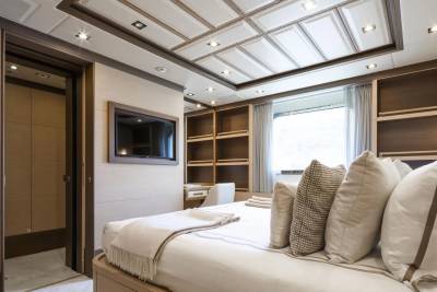 A luxurious yacht cabin features a comfortable bed, built-in shelving, and a wall-mounted television.
