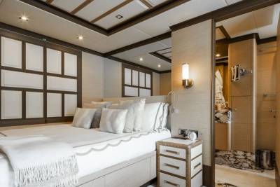 Luxurious yacht cabin features a plush bed, elegant wall paneling, and an adjoining marble-accented bathroom.