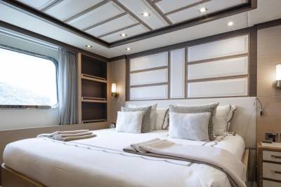 Luxurious yacht cabin features a plush bed, elegant wall paneling, and a large window with scenic views.