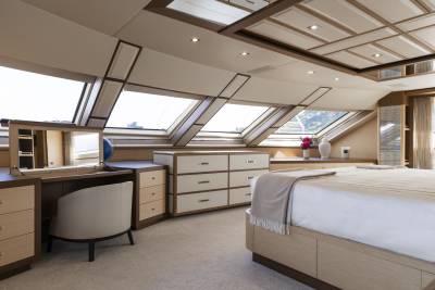 A luxurious bedroom features a vanity, dresser, and bed beneath angled skylights offering a glimpse of the outdoors.