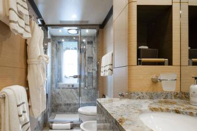Luxurious robes and plush towels await in this elegantly appointed yacht bathroom featuring marble accents and a glass-enclosed shower.